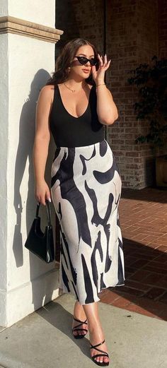 Woman in a black top and patterned pleated skirt holding sunglasses