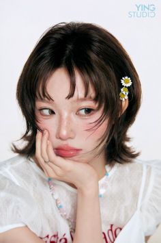 Woman with short hair and freckles, wearing a white top and daisy flowers in her hair