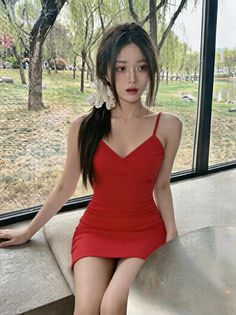 Woman in a red dress with long hair sitting by a window with outdoor view