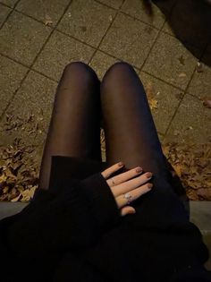 Person wearing black tights and a dark sweater, with rings on their fingers