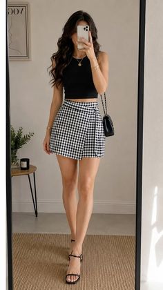 Woman in a black crop top and gingham skirt taking a mirror selfie