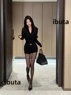 Woman in a black outfit and tights walking indoors with a handbag