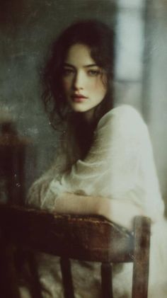 Woman with long dark hair in a white dress, leaning on a chair