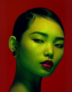 Woman with green skin and red lipstick against a red background