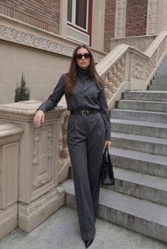Woman in a gray suit and sunglasses standing on a stone staircase