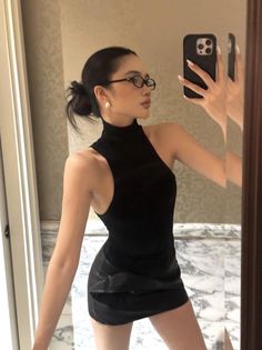 Woman in a black top and mini skirt taking a mirror selfie