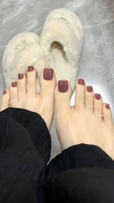 Feet with burgundy painted toenails and fluffy slippers on a tiled floor
