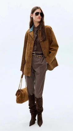 Woman in a brown jacket, sunglasses, and boots holding a shoulder bag