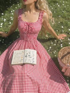 Woman in a red gingham dress sitting in a daisy field with an open book