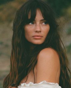 Woman with long hair and freckles looking away, with exposed shoulders