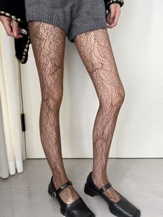 Person wearing lace tights, grey shorts, and black mary jane shoes indoors