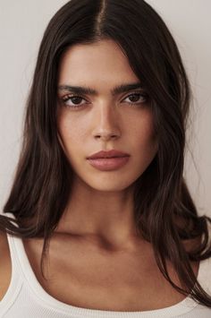 Woman with long dark hair wearing a white top, looking directly at the camera