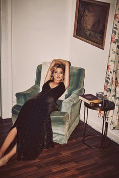 Woman in a black dress with a slit, reclining in an armchair indoors