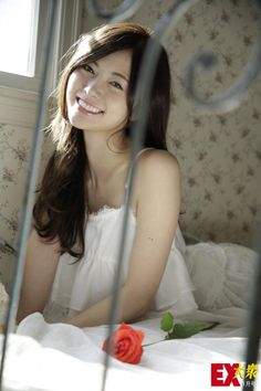 Smiling woman with long hair in a white dress in a sunlit bedroom