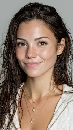 Woman with wet hair, freckles, and layered gold necklaces smiling at the camera