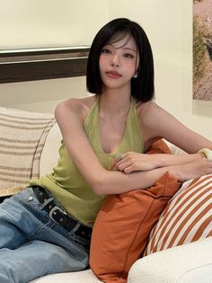 Woman with short black hair wearing a green halter top and jeans on a couch