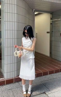 Woman in a white top and polka dot skirt holding a small handbag outdoors