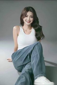 Woman with long hair wearing a white tank top and loose pants, sitting indoors
