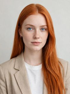 Woman with long red hair and blue eyes wearing a beige blazer and white t-shirt