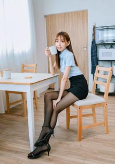 Woman in a light blue shirt and black mini skirt holding a mug indoors