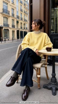 Woman in a yellow sweatshirt and dark jeans sitting at an outdoor cafe