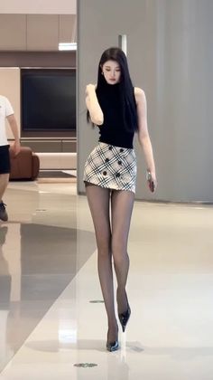 Woman with long black hair wearing a black top and plaid skirt indoors