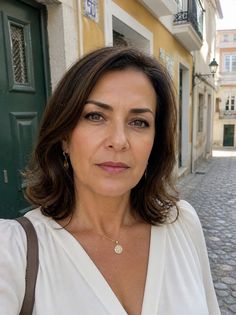 Woman with short brown hair wearing a white blouse and gold jewelry on a cobblestone street