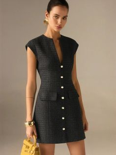 Woman in a dark tweed dress with gold accessories holding a yellow handbag