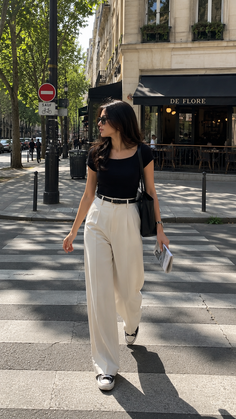 Woman in a black top and wide leg pants crossing a street in a city