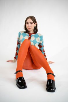 Woman in an argyle cardigan and orange tights sitting on a white background