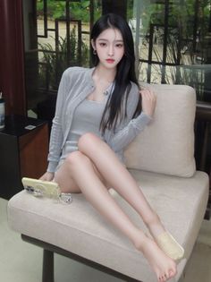 Woman with long black hair wearing a gray cardigan and mini dress, sitting indoors