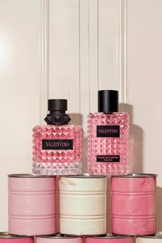 Two Valentino perfume bottles with pink liquid on stacked pink and white cans