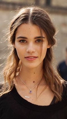 Young woman with long brown hair and freckles wearing silver necklaces outdoors