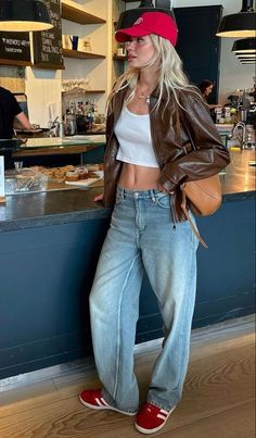 Blonde woman in a red cap, brown leather jacket, and crop top in a cafe