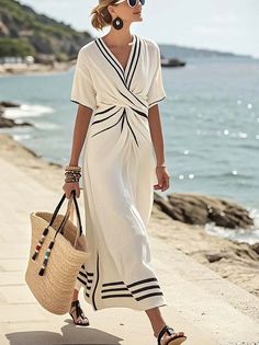 Woman in a white dress with black stripes walking along a beach path