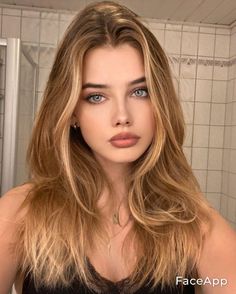 Woman with long blonde hair and blue eyes wearing a black top indoors