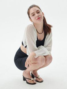 Woman in a white cardigan and black crop top squatting in a studio