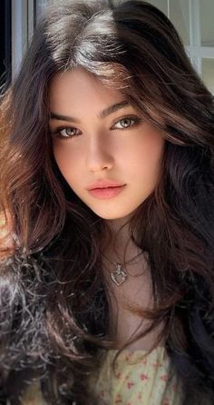 Woman with long brown hair and a heart necklace, lit by soft natural light