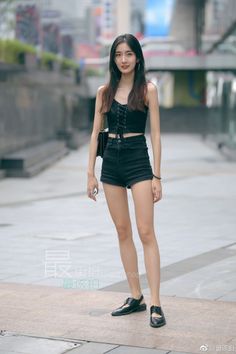 Woman in a black crop top and denim shorts standing on a street