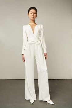 Woman in a white jumpsuit with a pearl necklace posing in a studio