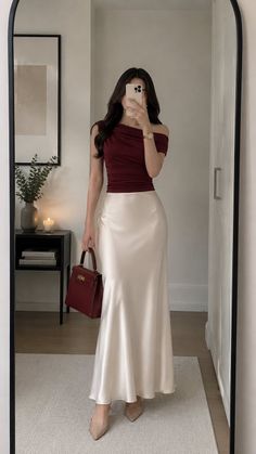 Woman in an off-shoulder top and satin skirt taking a mirror selfie indoors
