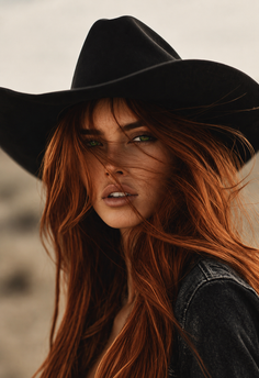 Woman with long red hair and green eyes wearing a cowboy hat and denim jacket
