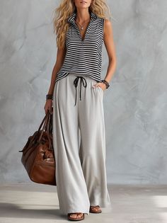 Woman with long blonde hair wearing a striped top and wide leg pants, holding a brown bag