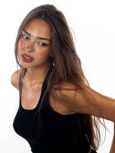 Woman with long brown hair and a black tank top against a white background