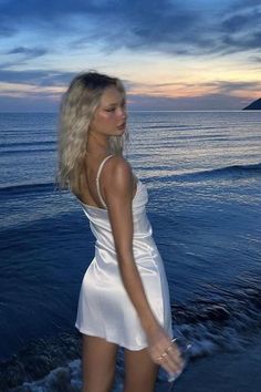 Woman in a white dress standing in the water at sunset