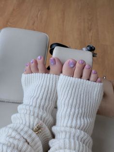 Feet with purple painted toenails wearing white leg warmers and jewelry