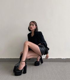 Woman in a black blazer and leather skirt squatting indoors