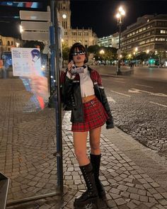 Woman in a plaid skirt and leather jacket holding a camcorder at night