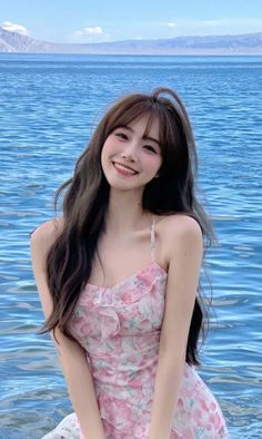 Woman in a pink floral dress smiling by blue water with mountains in the background
