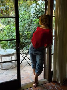 Woman in a red top and blue jeans standing in a doorway looking out to a patio